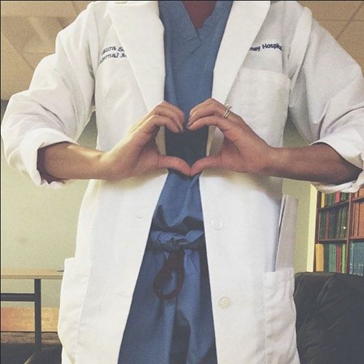 a man in a lab coat making a heart with his hands while standing next to a bookcase