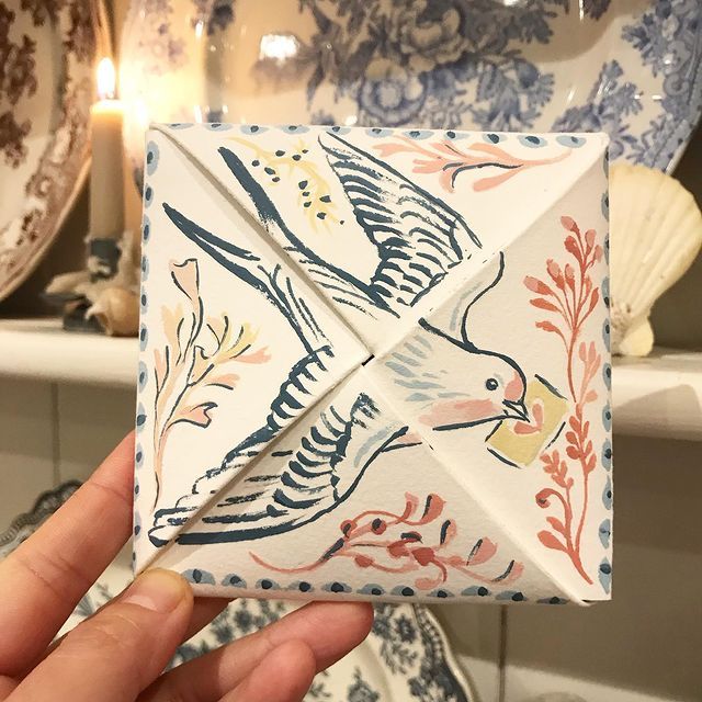 a hand holding an origami bird in front of some plates and candles on a shelf