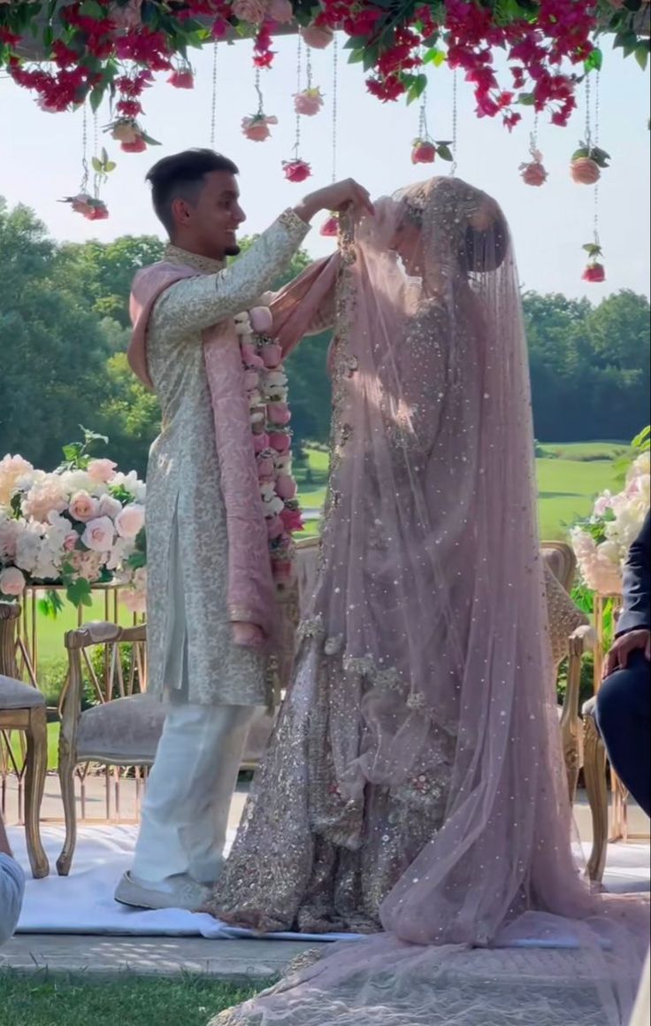 a man and woman standing next to each other in front of a flower covered archway