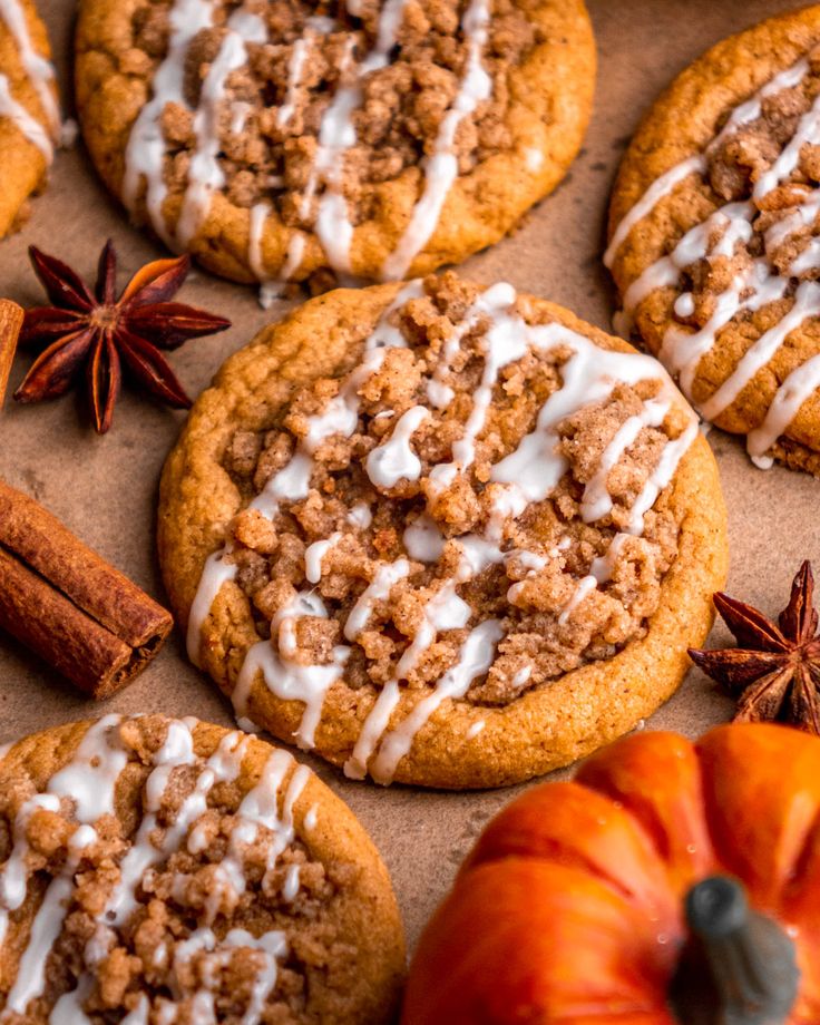 several cookies with white icing and cinnamon on top, next to an orange pumpkin