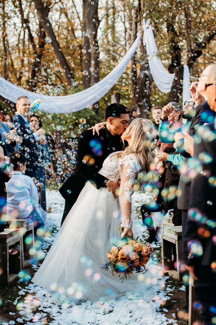 a bride and groom are kissing under bubbles as they walk down the aisle at their wedding