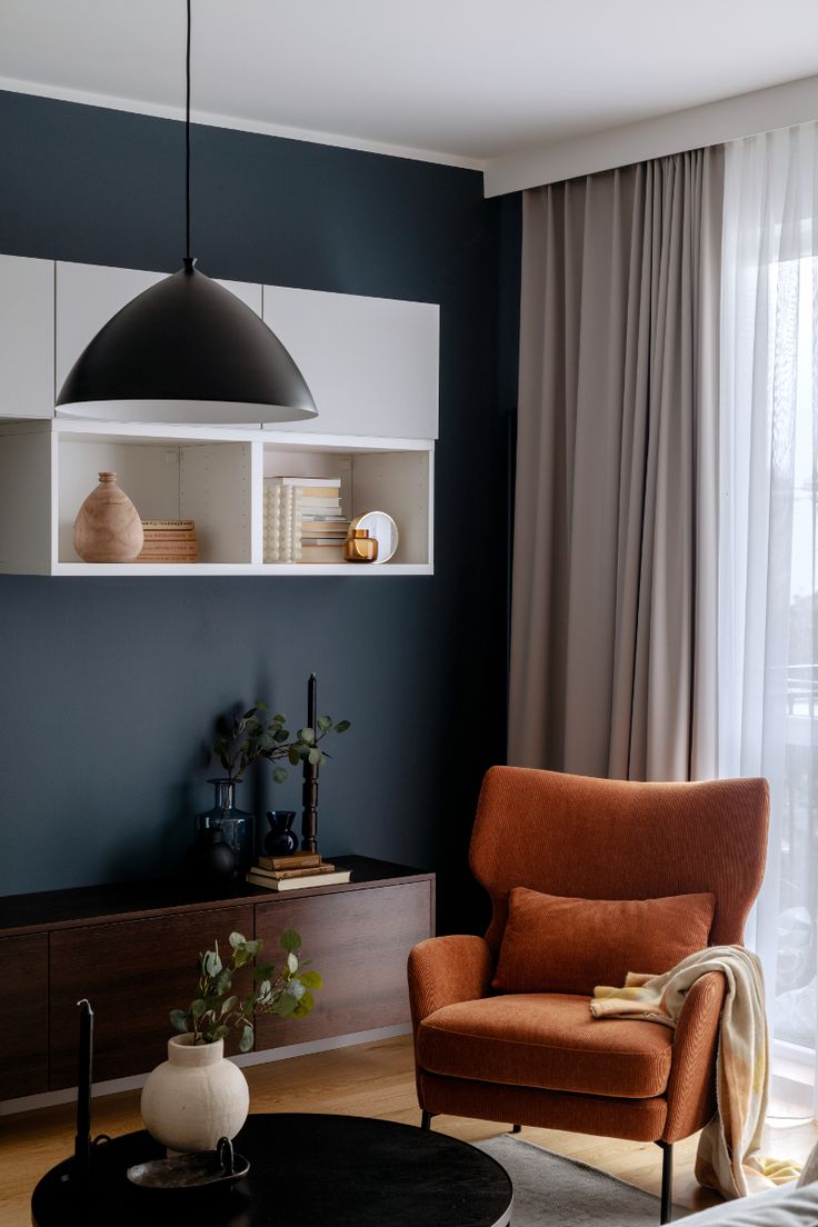 an orange chair sitting in front of a window next to a black and white wall