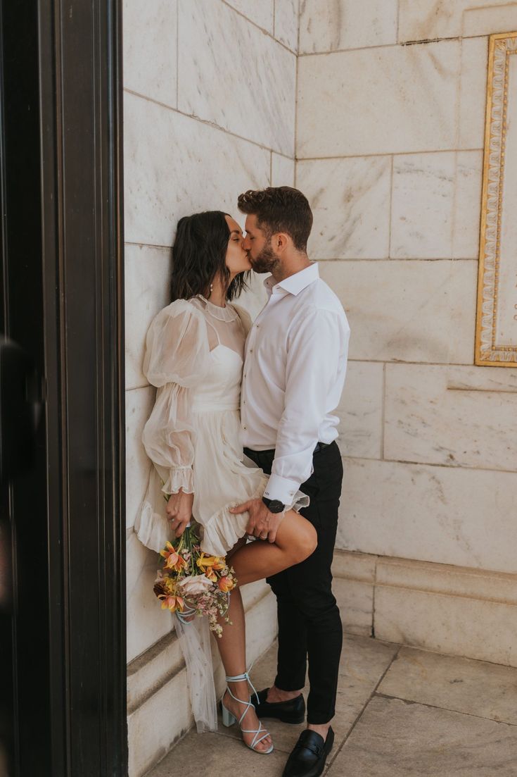 a man and woman standing next to each other in front of a wall with flowers