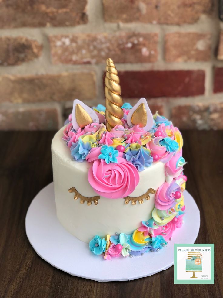 a white cake with pink, yellow and blue frosting has a unicorn horn on top