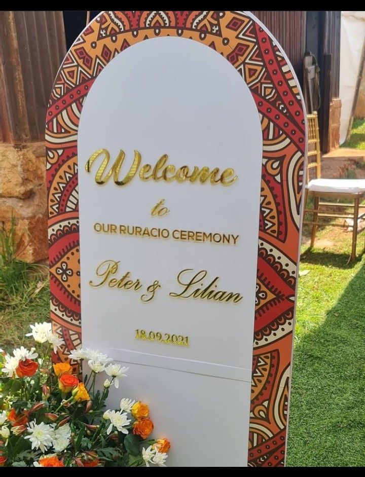 a welcome sign with flowers in the foreground and an orange, yellow, and white background