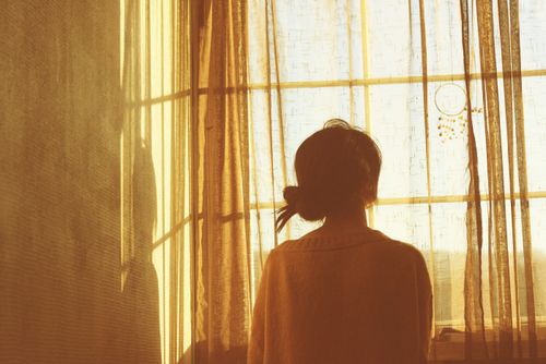 a woman standing in front of a window looking out at the sun shining through it