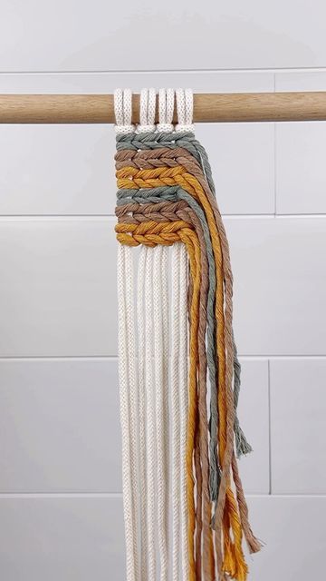 multicolored macrame wall hanging with wooden bar on white tiled wall background