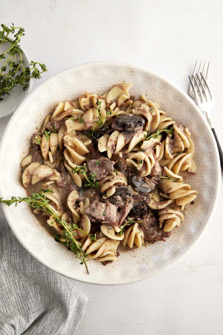 a white bowl filled with pasta and mushrooms on top of a table next to silverware