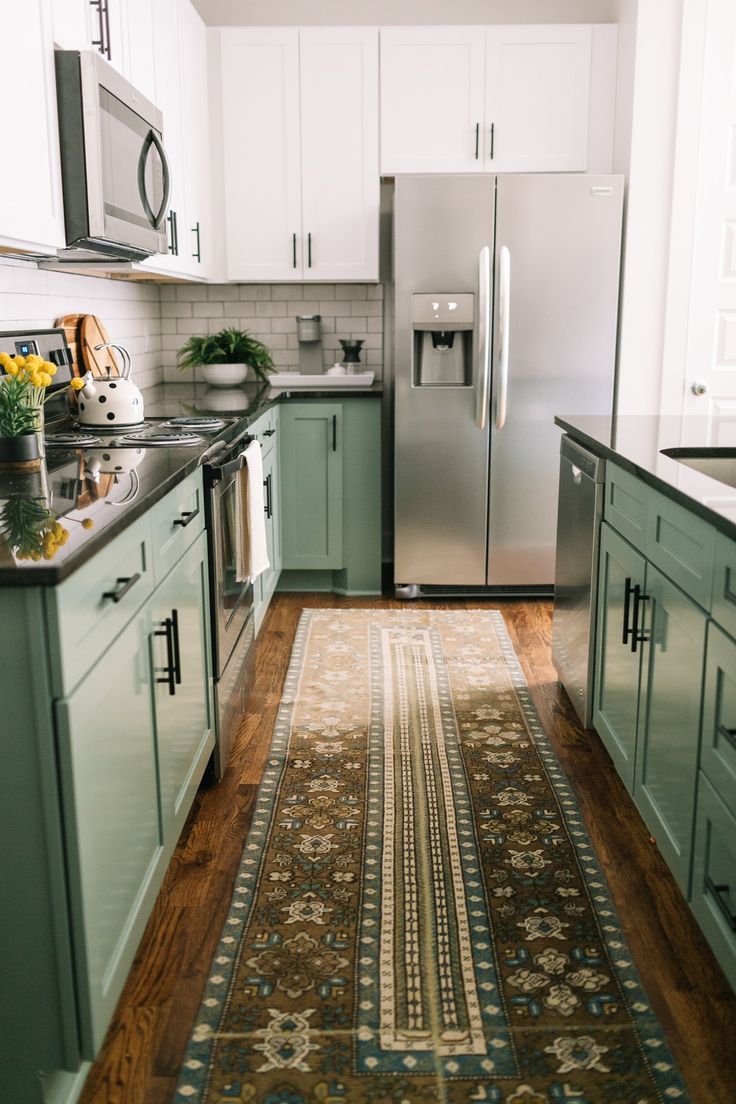 a kitchen with green cabinets and a rug on the floor in front of the refrigerator