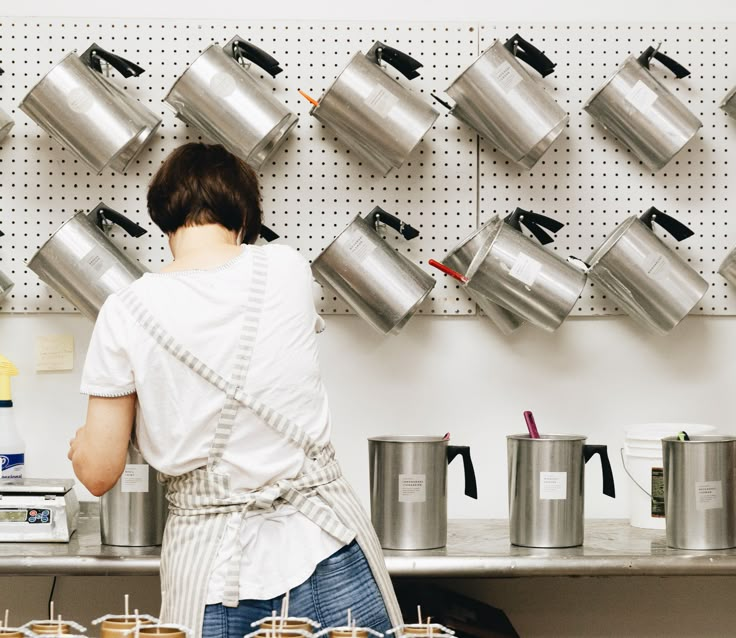 a woman standing in front of a counter filled with pots and pans on the wall