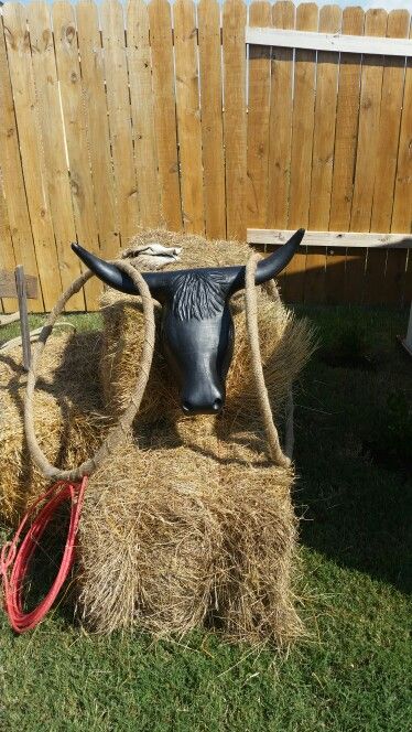 a fake cow head sitting on top of hay bales in front of a fence