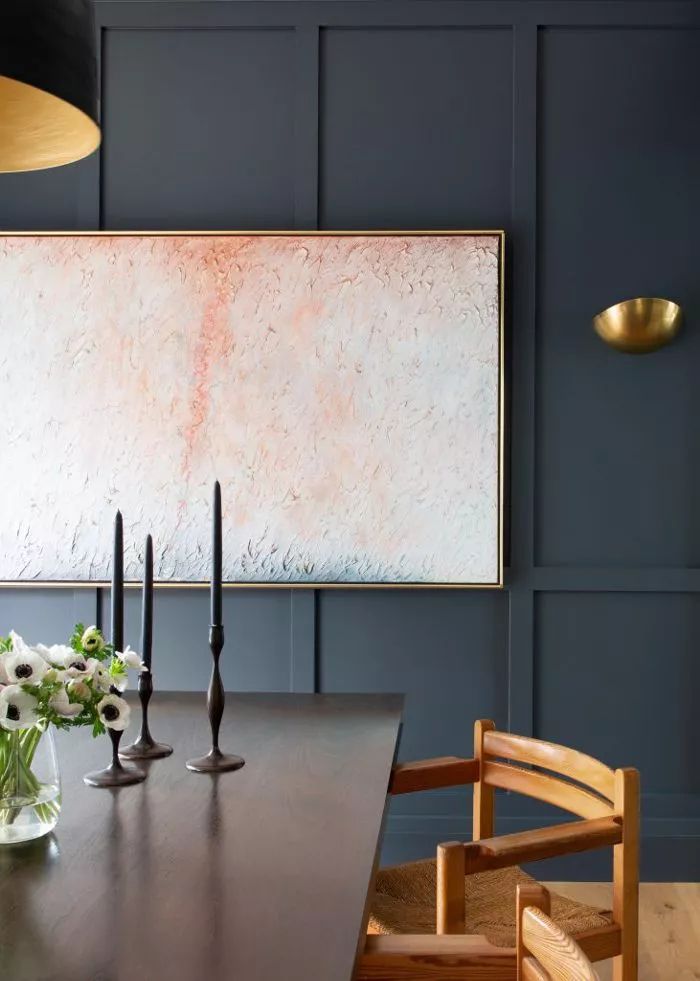 a dining room table with candles and flowers in vases next to a large painting on the wall