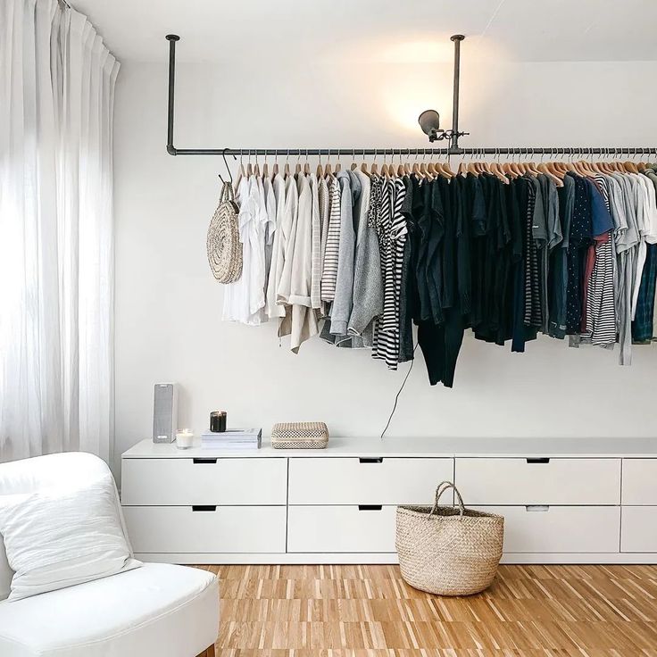 an organized closet with clothes hanging on the rack and a white chair in front of it