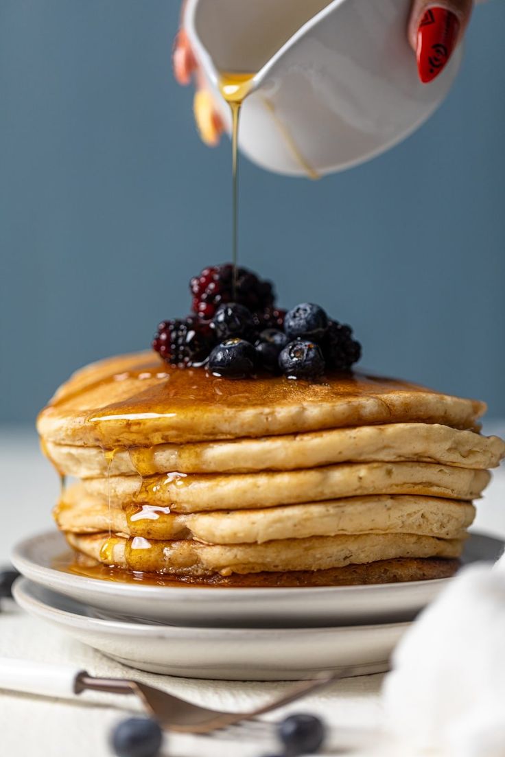 a stack of pancakes with syrup being drizzled over them and topped with berries