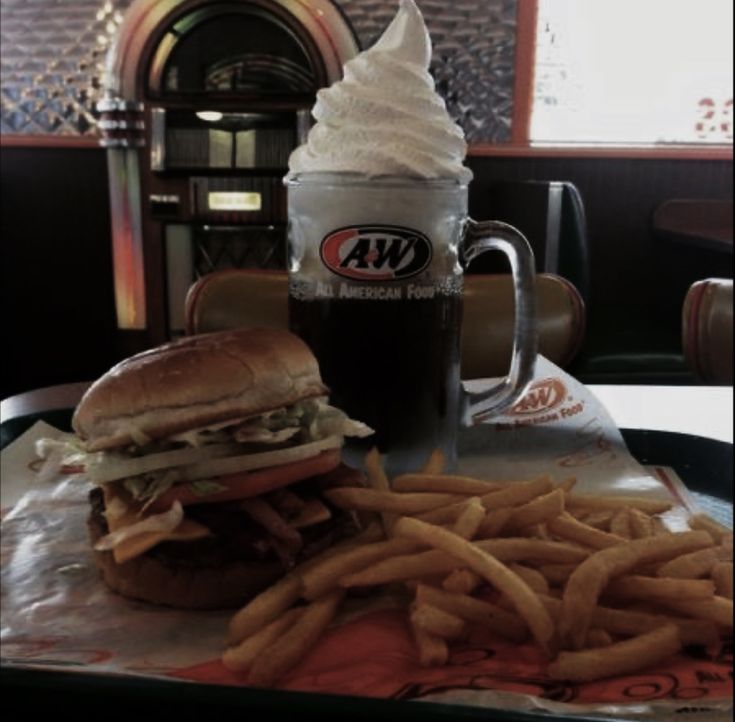 a sandwich and french fries on a tray with a cup of ice cream in the background