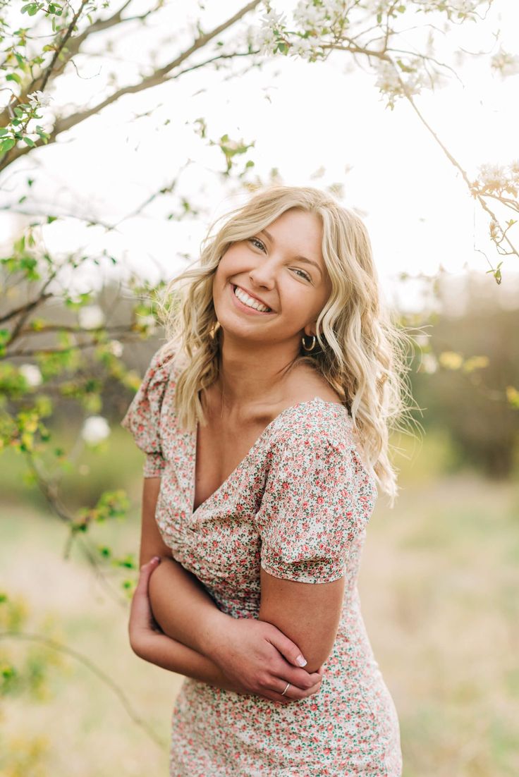 a woman standing in front of a tree with her arms crossed and smiling at the camera