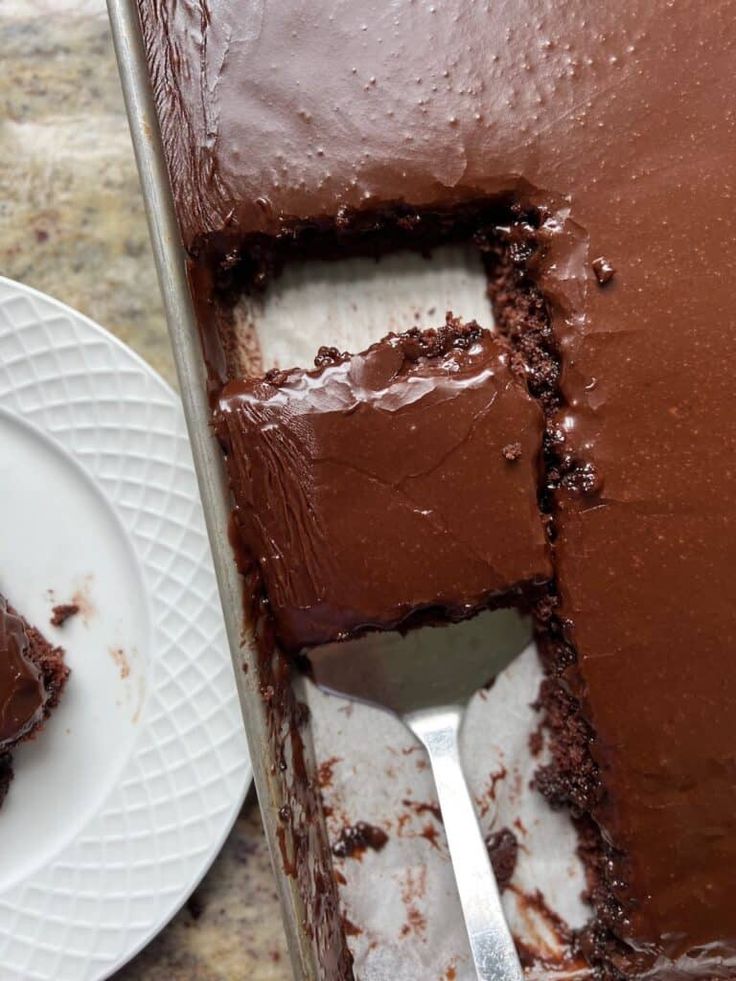 a piece of chocolate cake on a white plate with a fork in it next to the rest of the cake