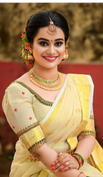 a woman wearing a yellow and white sari sitting on the ground with her hands clasped