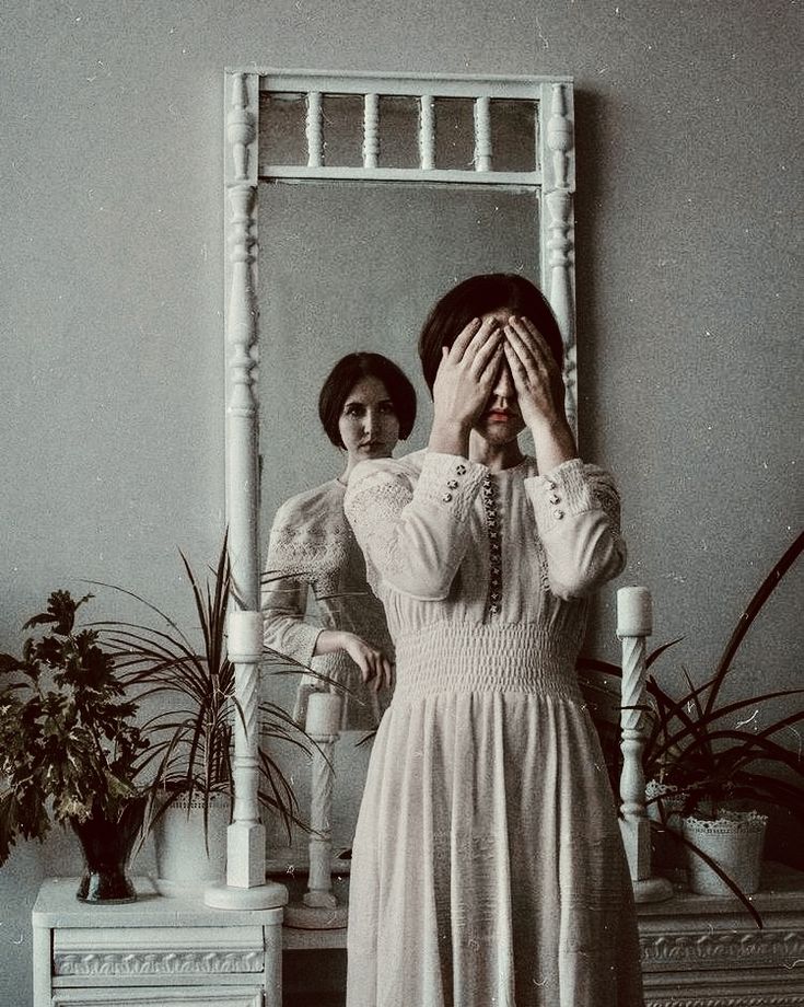 a woman standing in front of a mirror covering her eyes