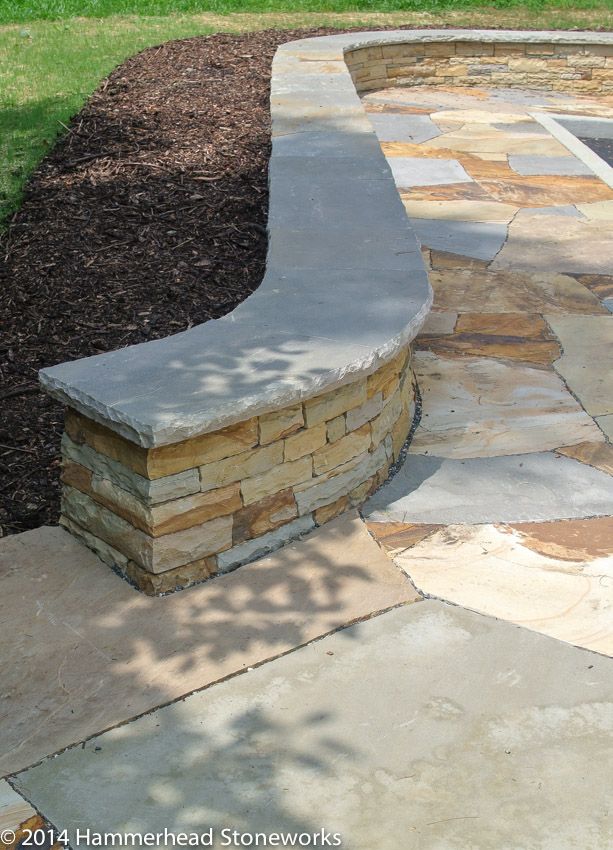 a stone bench sitting in the middle of a yard next to a fire pit and grass