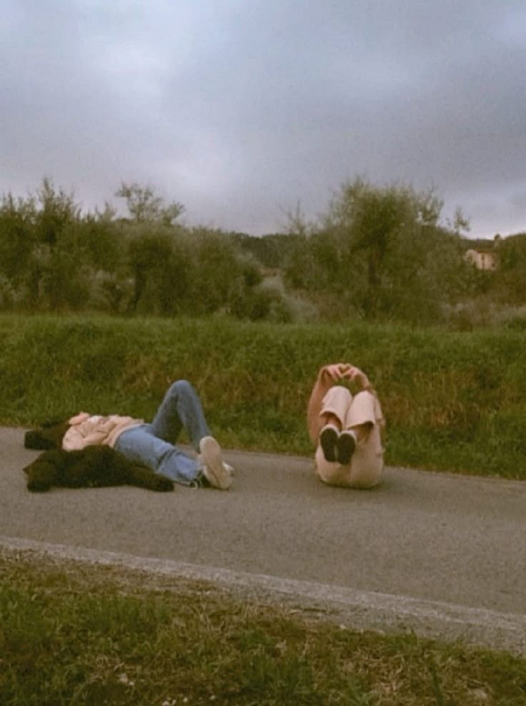 two people laying on the side of a road with their feet up in the air