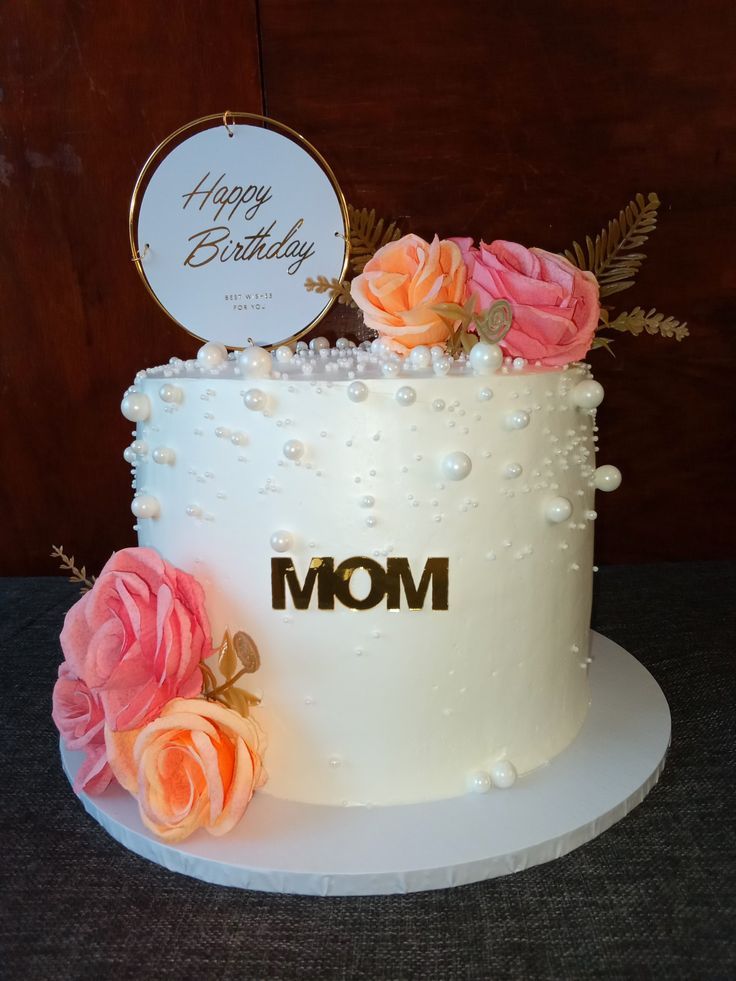 a white cake with pink flowers and a happy birthday sign on top that says mom