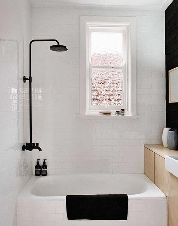 an image of a white bathroom with black and white accessories on the tub, window above it