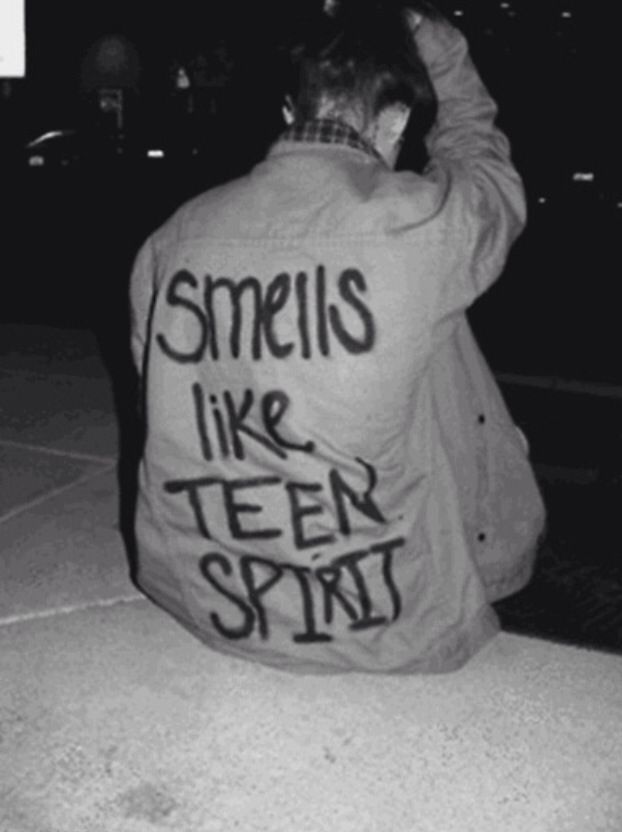 a man sitting on the sidewalk wearing a jacket that says smells like tear spirit