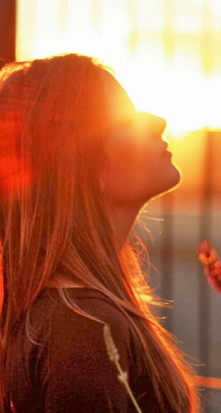 a woman standing in front of the sun with her hair blowing back and eyes closed