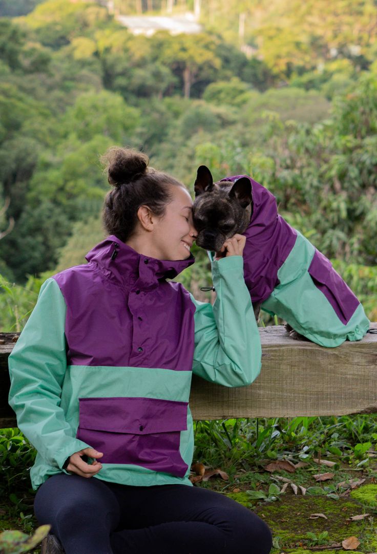 a woman is sitting on a bench with her dog wearing purple and teal jackets