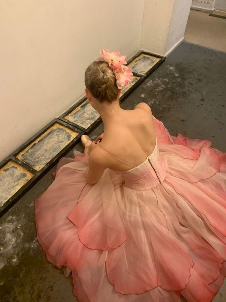 a woman in a pink dress sitting on the floor with her back to the camera