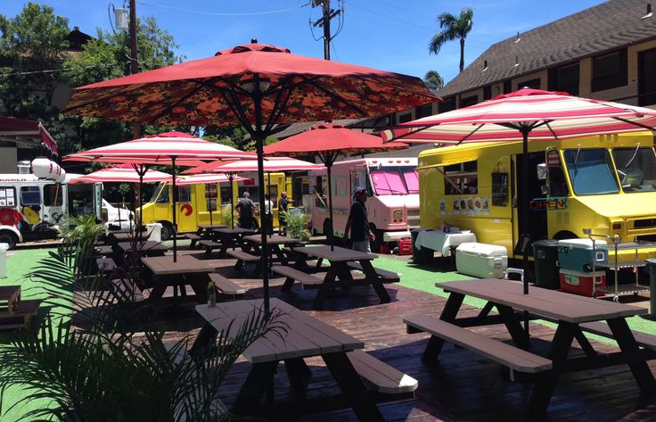 food trucks are lined up with umbrellas and picnic tables in front of the building