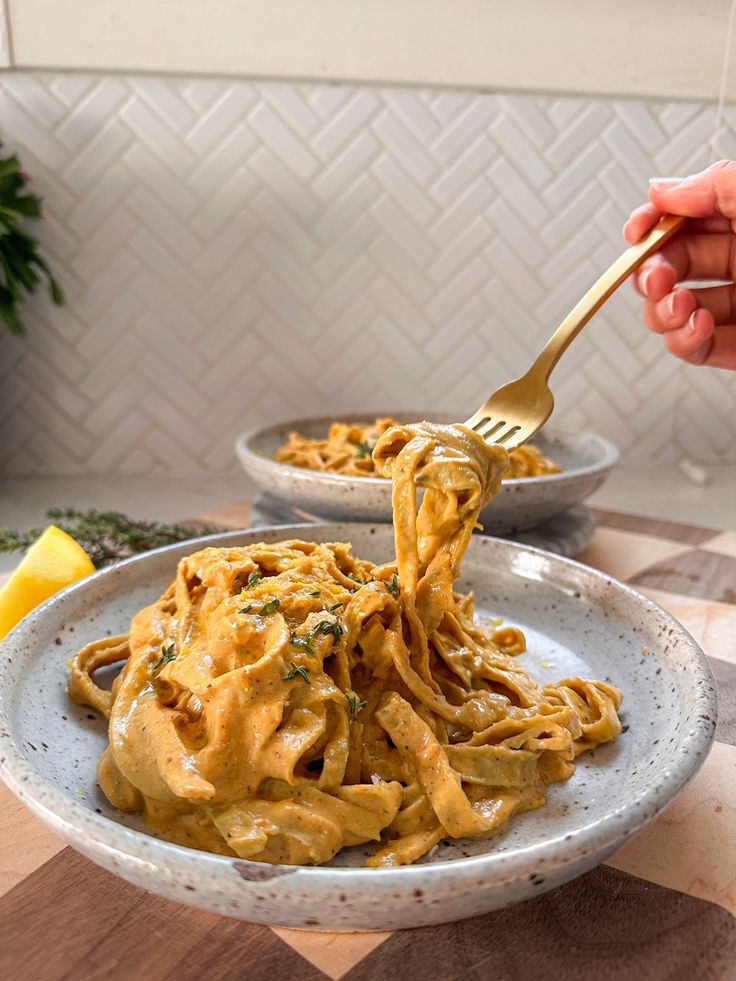 a person is holding a fork full of pasta in a white bowl on a wooden table