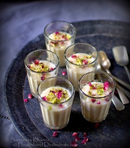 four glasses filled with dessert sitting on top of a blue plate next to spoons