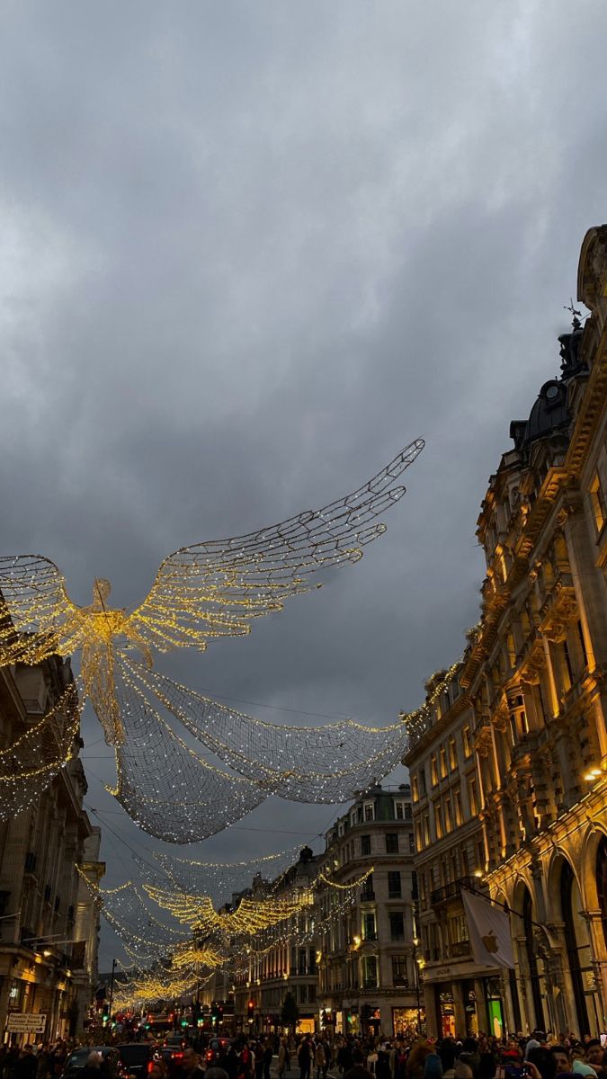 people are walking down the street in front of buildings with christmas lights strung from them