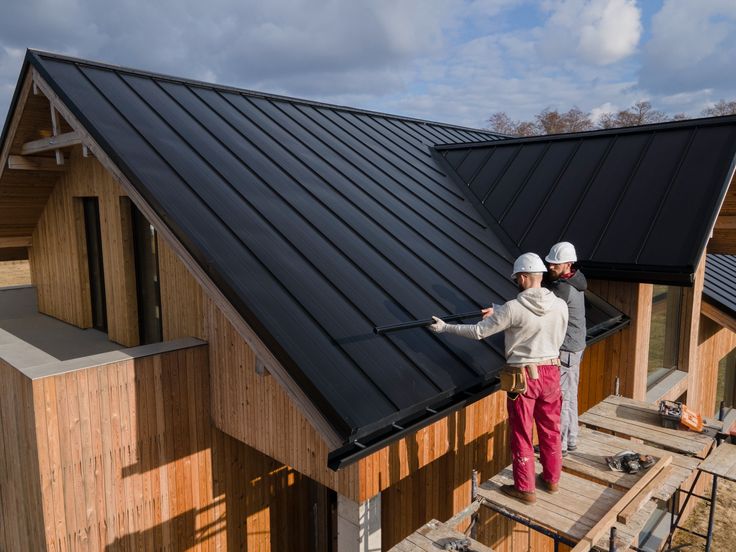 two men are standing on the roof of a wooden house while one man is fixing the shingles