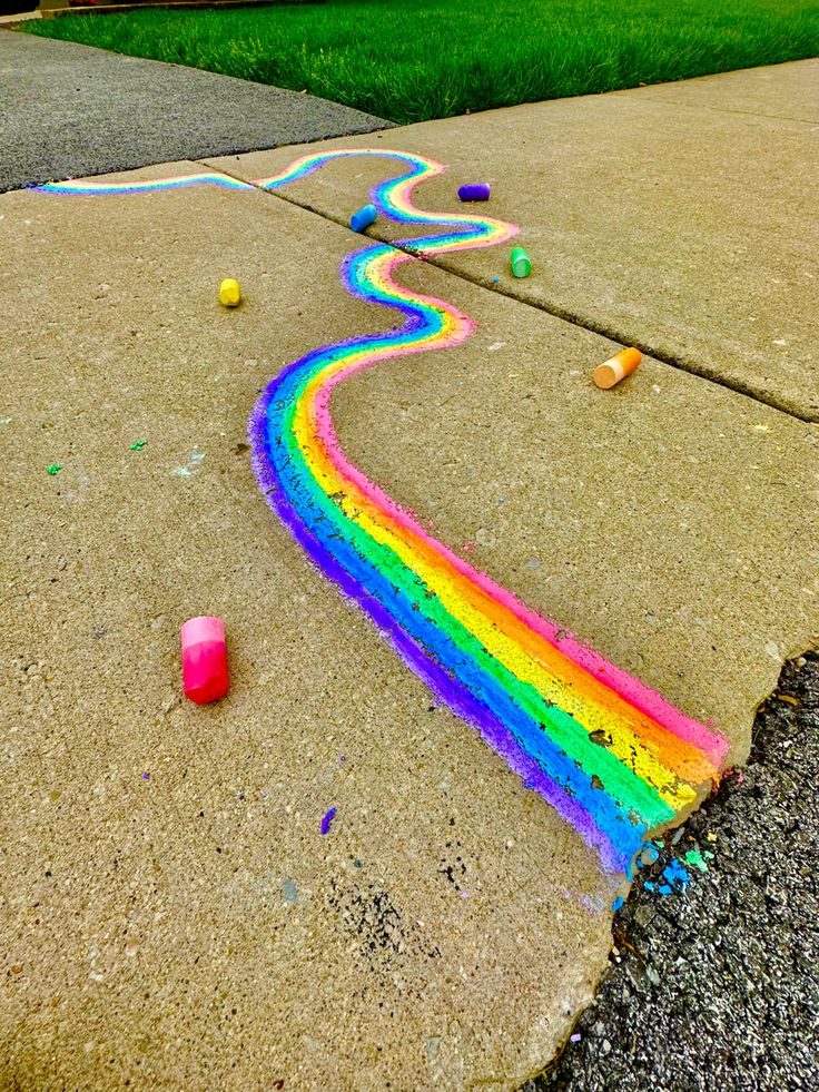 a rainbow painted sidewalk with balls and crayons on the ground next to it