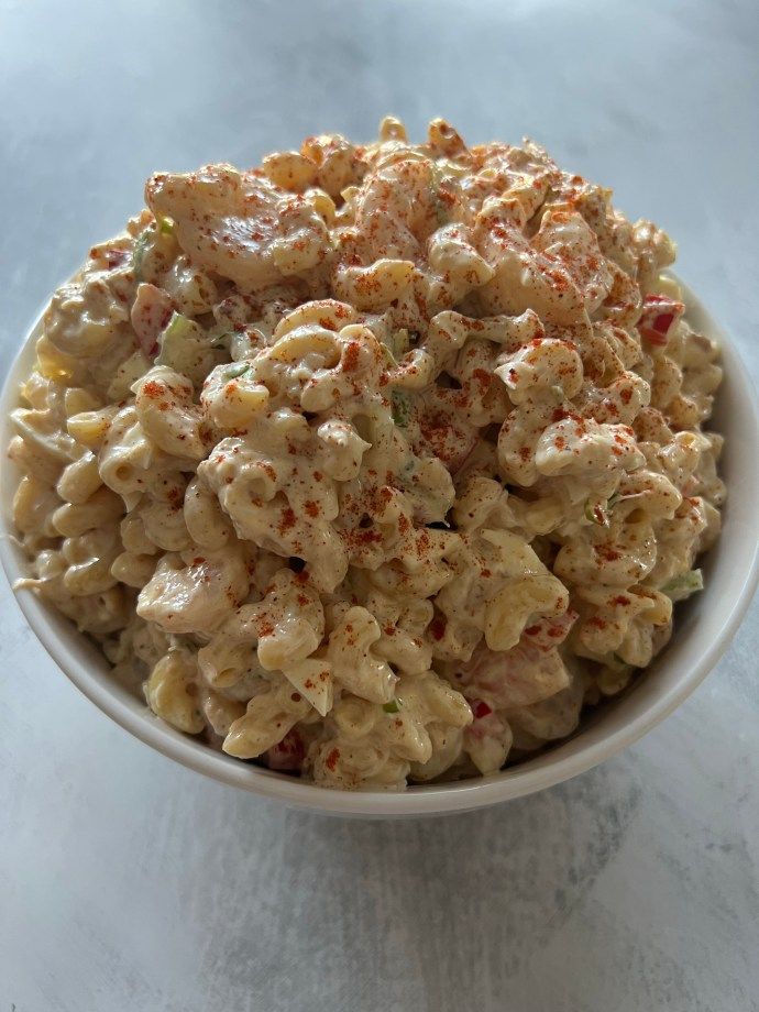 a white bowl filled with macaroni salad on top of a table next to a fork