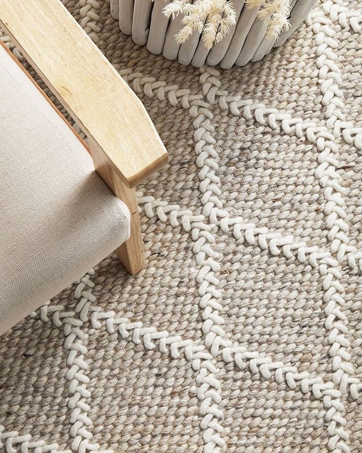 a close up of a rug on the floor with a chair and vase in the background