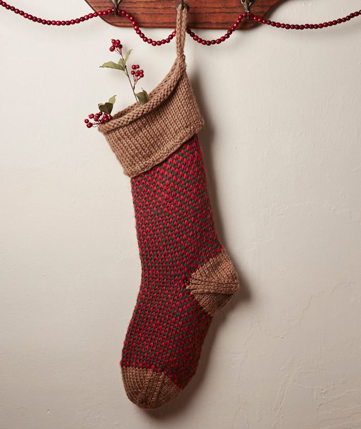 a knitted christmas stocking hanging from a wooden hanger on a white wall