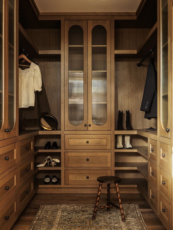 a walk in closet filled with lots of wooden drawers and shelves next to a rug