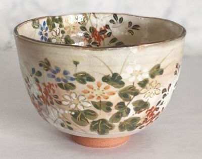 a bowl with flowers painted on it sitting on a white tableclothed surface, in front of a marble wall