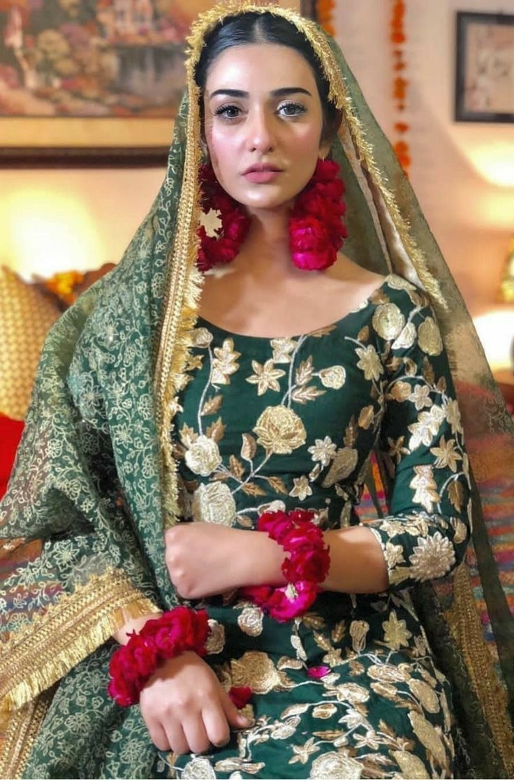 a woman sitting on top of a bed wearing a green and gold dress with flowers in her hair