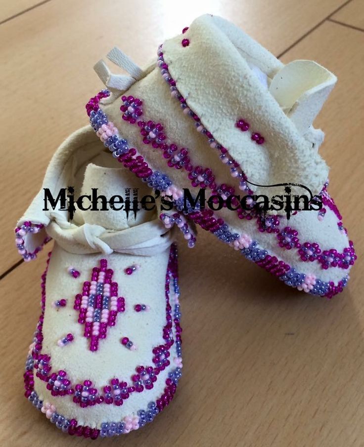 a pair of white shoes with pink and purple beads on them sitting on top of a wooden floor