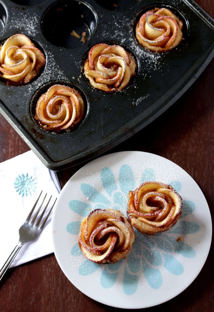 some cinnamon rolls are on a plate next to a muffin tin with one bite taken out