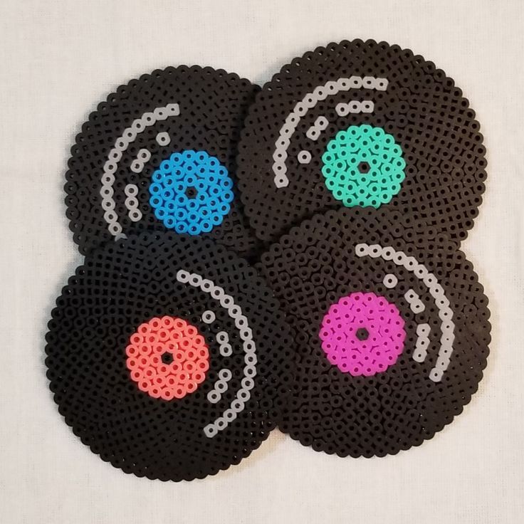 four black coasters with different colored circles on white cloth, each decorated with beading