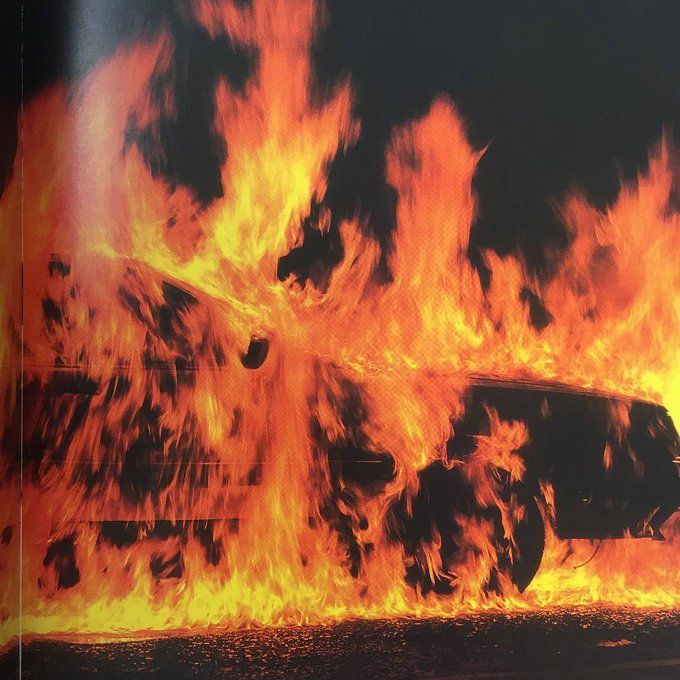 a car is on fire in front of a black background with red and yellow flames