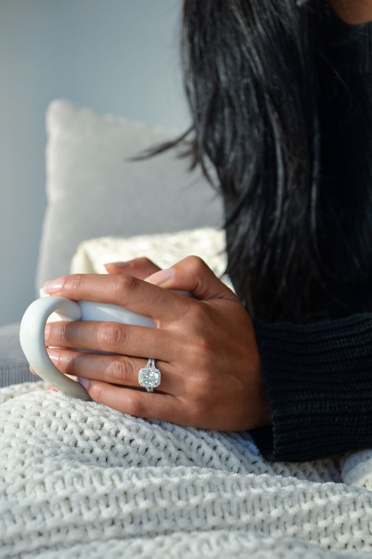 a woman is sitting on a couch holding her engagement ring