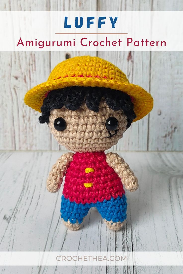 a small crocheted doll wearing a yellow hat and blue shorts with the words luffy on it