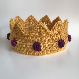 a crocheted yellow crown with purple pom poms